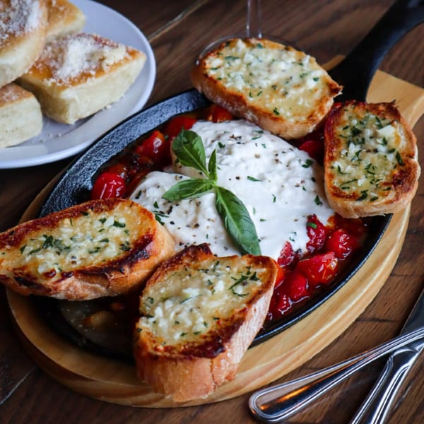 Bacco Centro's baked burrata with cherry tomatoes, basil, and garlic bread in a cast iron skillet.