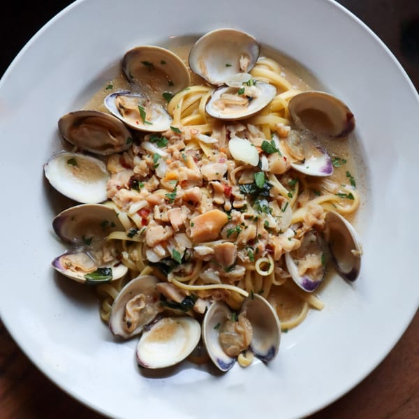 Linguine alle vongole with clams in shells, chopped clams, and parsley in a white bowl.