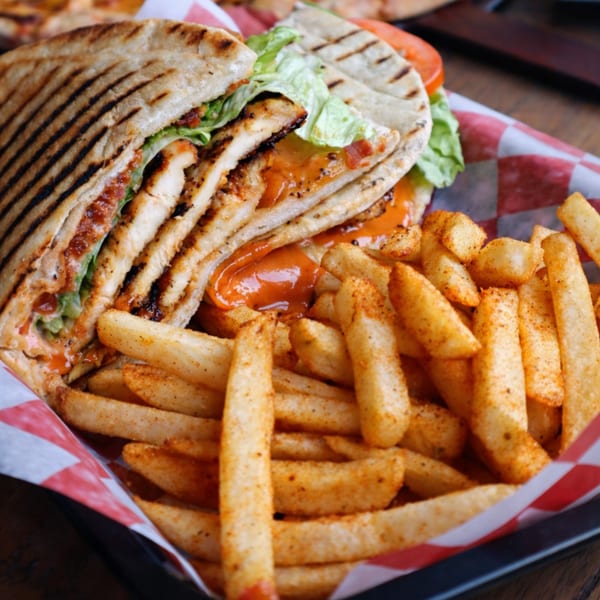 Grilled chicken panini with lettuce, tomato, and sauce, served with seasoned fries in a checkered basket.
