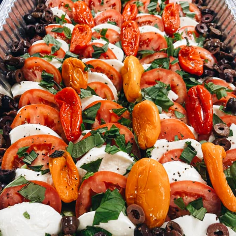 A vibrant Italian caprese salad with tomatoes, mozzarella, basil, olives, and roasted peppers.