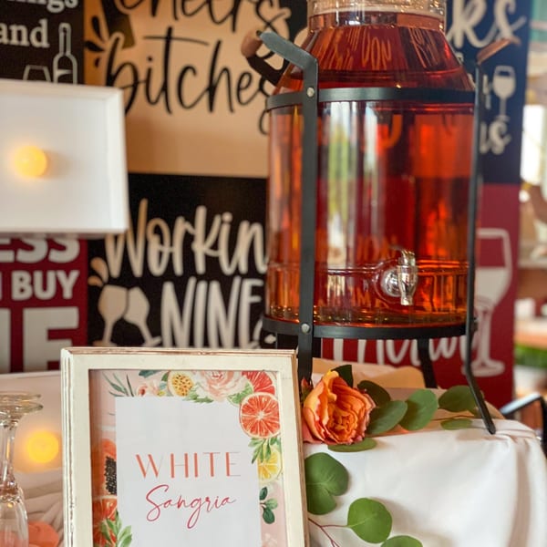 A large glass dispenser of red sangria sits next to a "White Sangria" sign and orange rose.