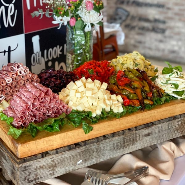 Italian antipasto platter with cured meats, cheeses, roasted peppers, and marinated artichokes on a wooden board.
